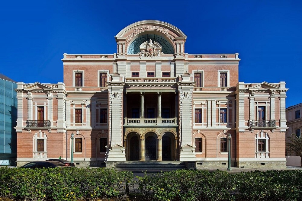 Fachada principal do Museu das Minas e do Metal, com duas grandes colunas, várias janelas, três andares e um brasão no alto onde se lê: "Secretaria da Educação".
