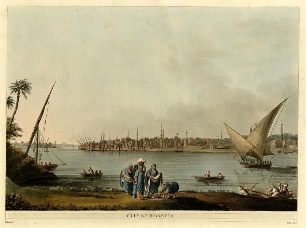 Ilustração antiga do Rio Nilo, com um grupo de mulheres em primeiro plano, pescadores e barcos à vela em segundo plano, a cidade de Rosetta com arquitetura otomana e minaretes ao fundo.