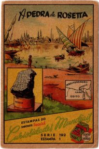 Reprodução de um cartão envelhecido, onde se lê em destaque: “Curiosidades Mundiais, A Pedra de Rosetta, Estampas do Sabonete Eucalol”. Em primeiro plano à esquerda, a ilustração apresenta um quadro com a Pedra de Rosetta em seu pedestal redondo, como era exposta no Museu Britânico. Outro quadro, à direita, mostra um mapa com a localização da cidade de Rosetta, no Egito. Em segundo plano, há uma paisagem bucólica do rio Nilo com barcos a vela, botes e pescadores. Ao fundo, na linha do horizonte, está a cidade de Rosetta, com edificações no estilo otomano, entremeadas por minaretes das suas mesquitas.Estampa ilustrada com a pedra de Rosetta no Museu Britânico em primeiro plano. Ao fundo, uma paisagem bucólica da cidade de Rosetta, com barcos, pescadores e edificações no horizonte.