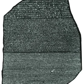 Texto da Pedra de Rosetta em branco com fundo preto, redigido em três idiomas: hieróglifos, demótico e grego antigo.